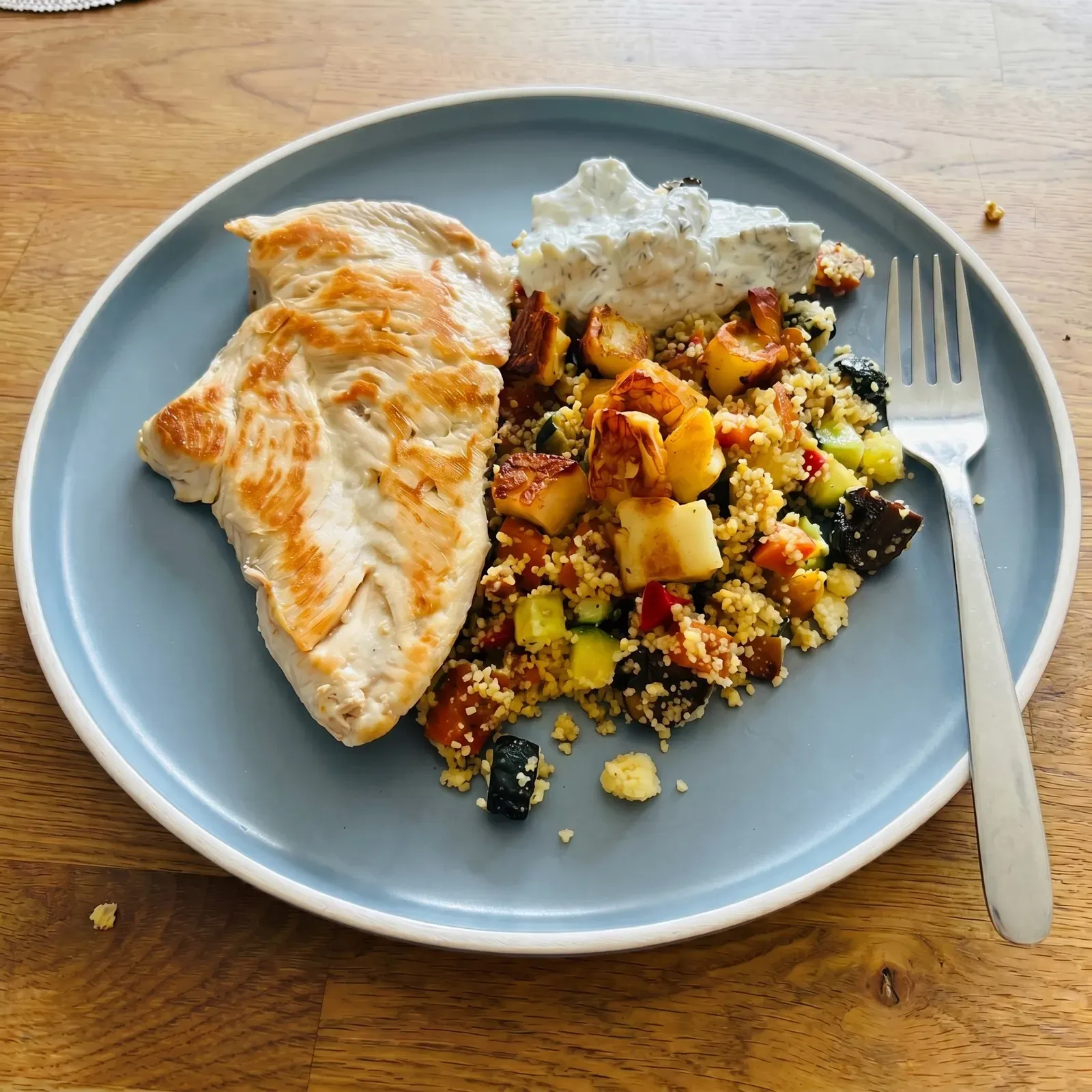 Mittagessen auf einem blauen Teller: gebratene Hähnchenbrust, Couscous mit buntem Ofengemüse und ein Kräuter-Dip